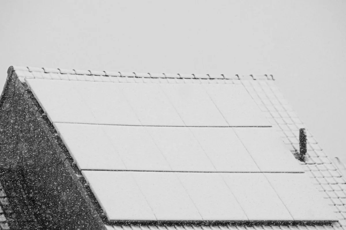 Toit de maison couvert de panneaux solaires recouverts de neige